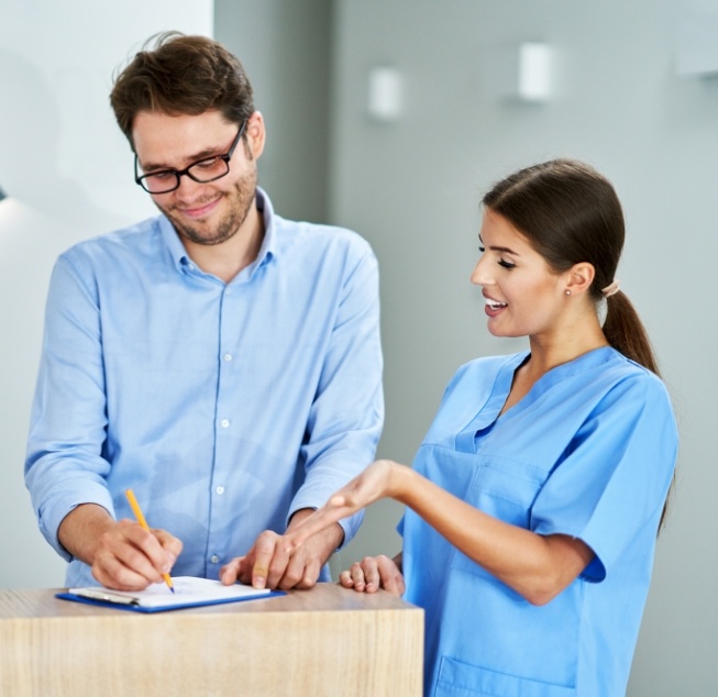 Dental team member showing a patient where to sign on a clipboard