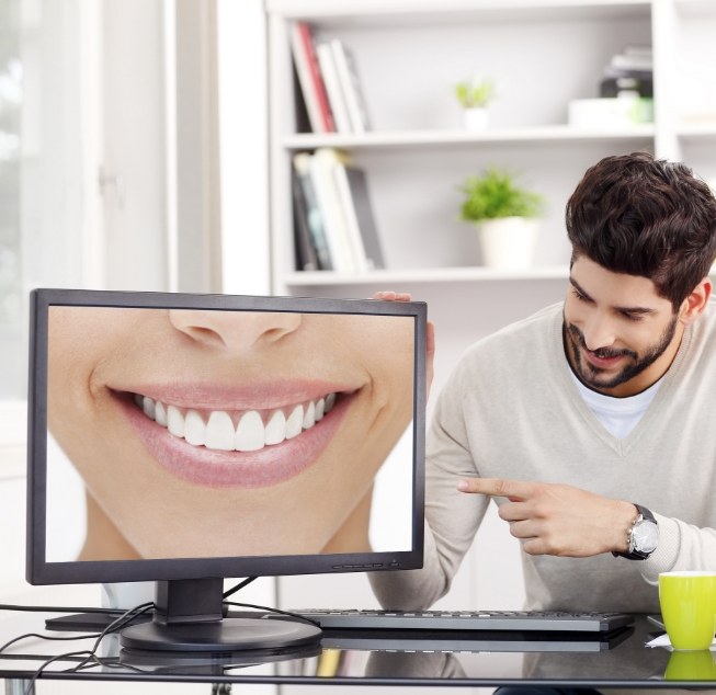Man gesturing to computer monitor showing close up of flawless smile
