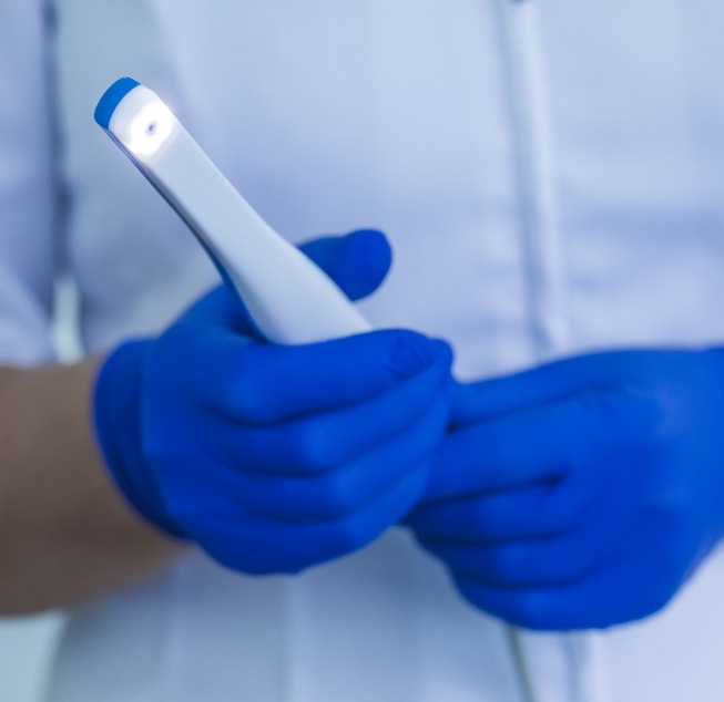 Gloved hand holding a thin white intraoral camera