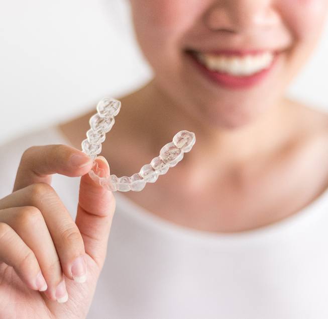 Smiling woman holding clear aligner