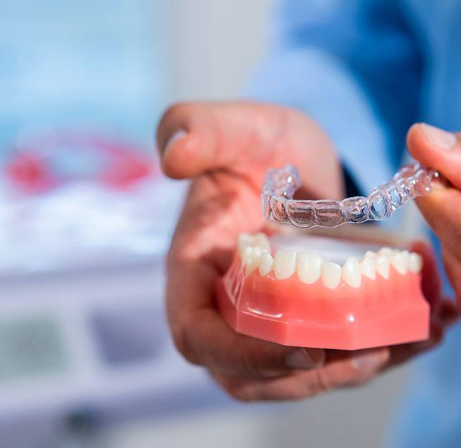Dentist putting clear aligner on model of teeth