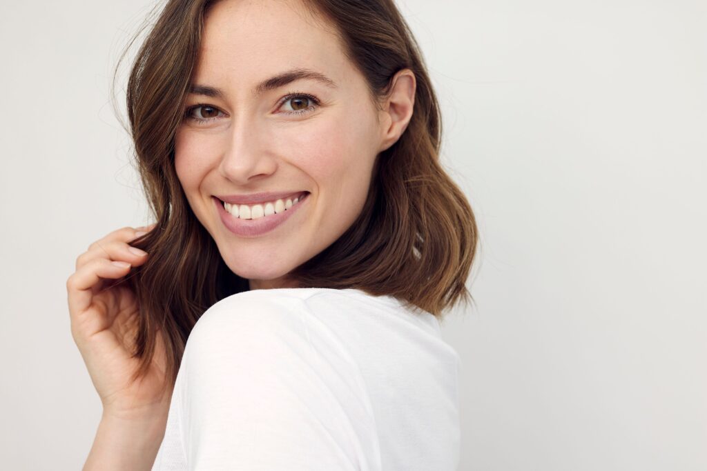 Woman with brown hair in white shirt smiling over her shoulder