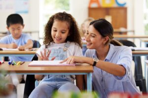 Teacher helping a young student in classroom.